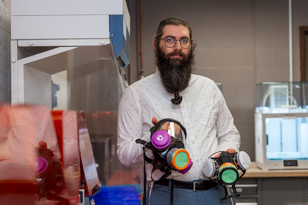 researcher holding two chemical respirator masks with covers over the valves.