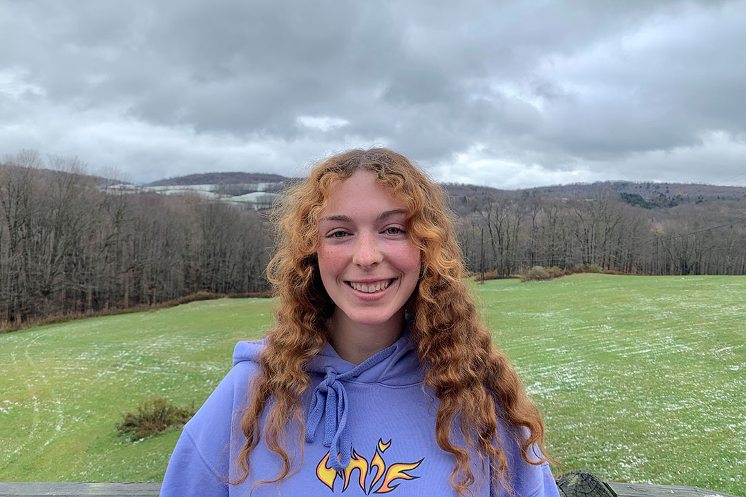 student standing at the top of a hill with trees in the background.