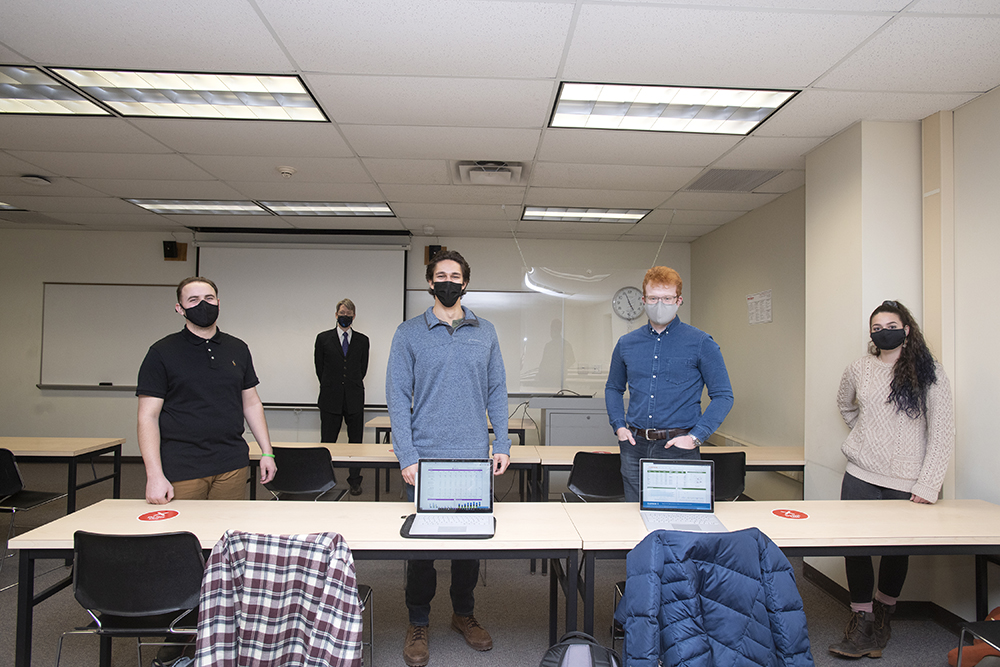 students and staff standing in masks behind table with computers.