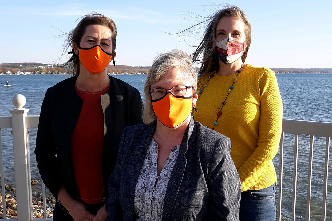 three women wearing fask masks standing on deck near a body of water.