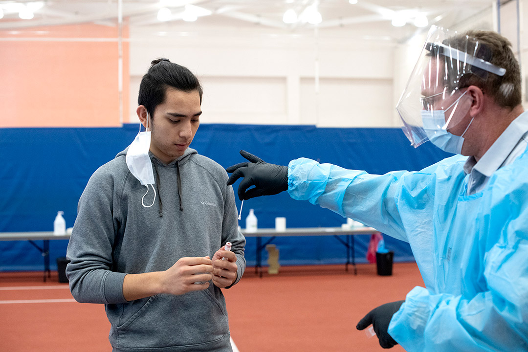 volunteer wearing PPE putting a swab into a vial that a student is holding.