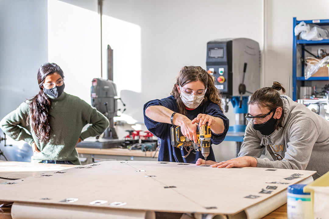 three students wearing masks and working with power tools.