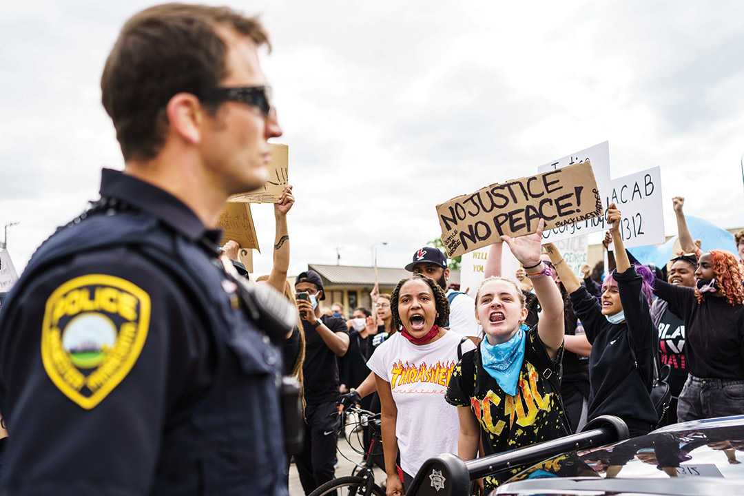 two young girls in a crowd yelling at a police officer during a protest.