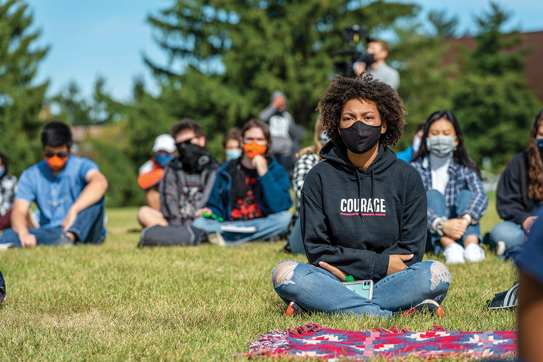 students wearing face masks and sitting socially distanced on a lawn.