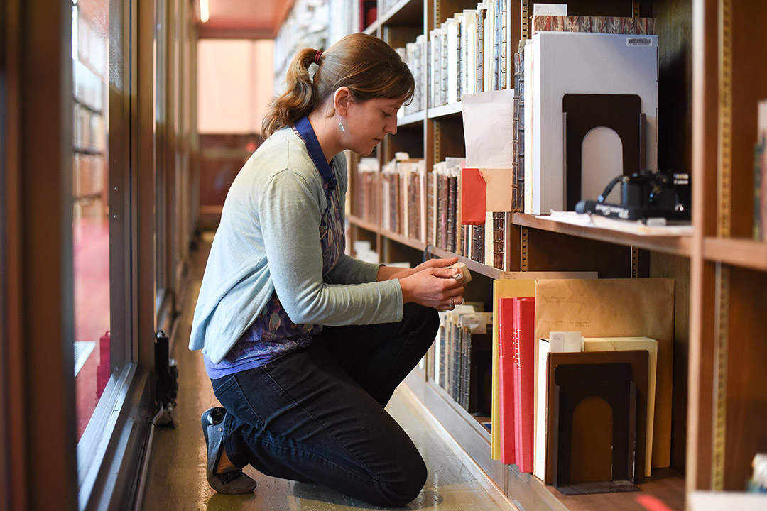 researcher examining row of books in a library.