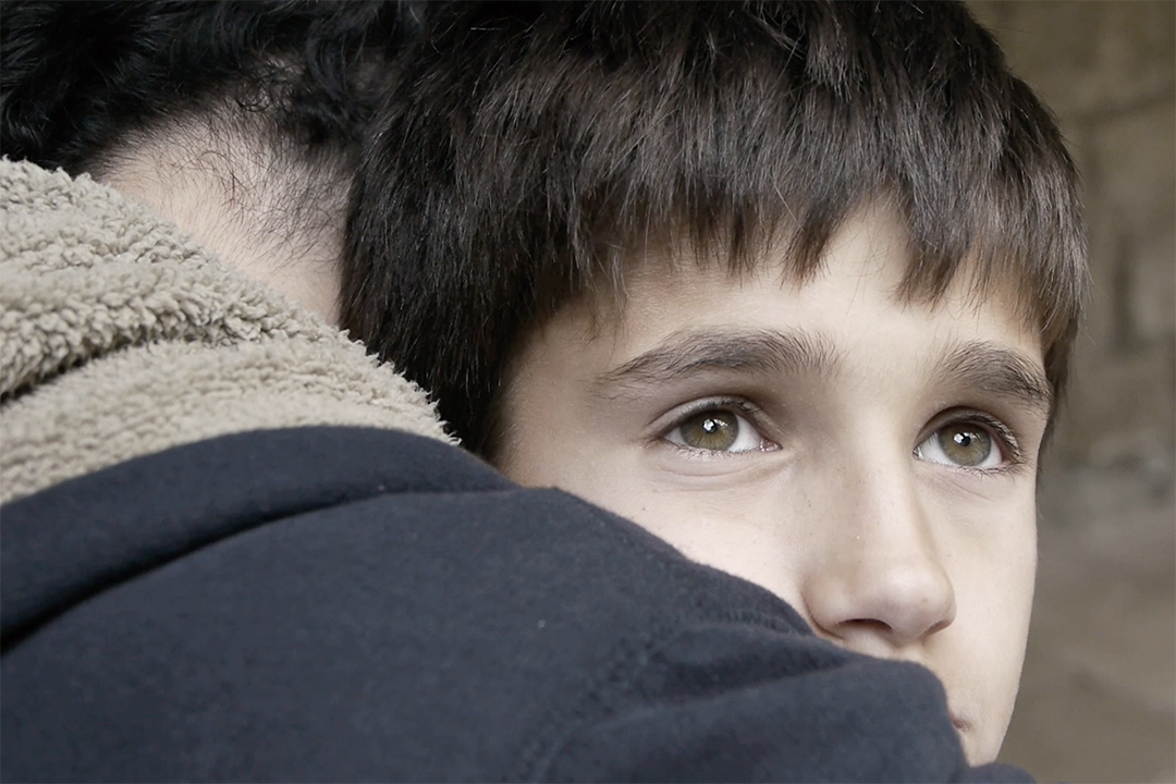 A boy looks off into the distance as he is embraced.