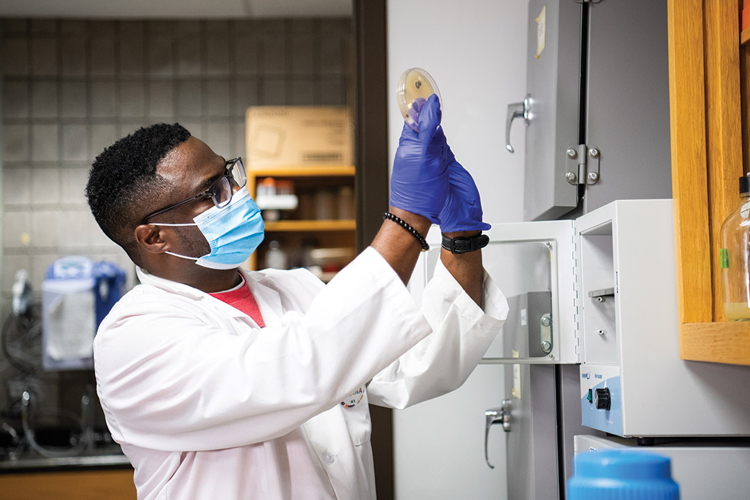 professor wearing labcoat and examining a grow on a petri dish.