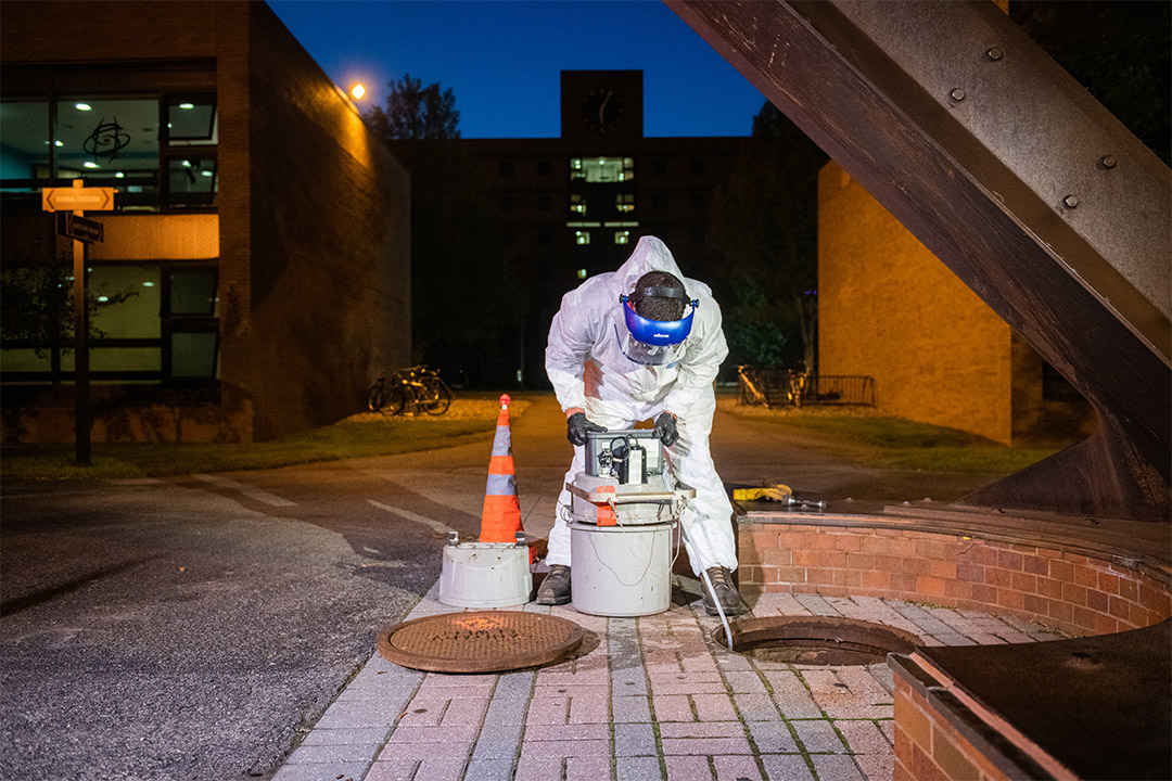 worker collecting wastewater sample from sewer system.