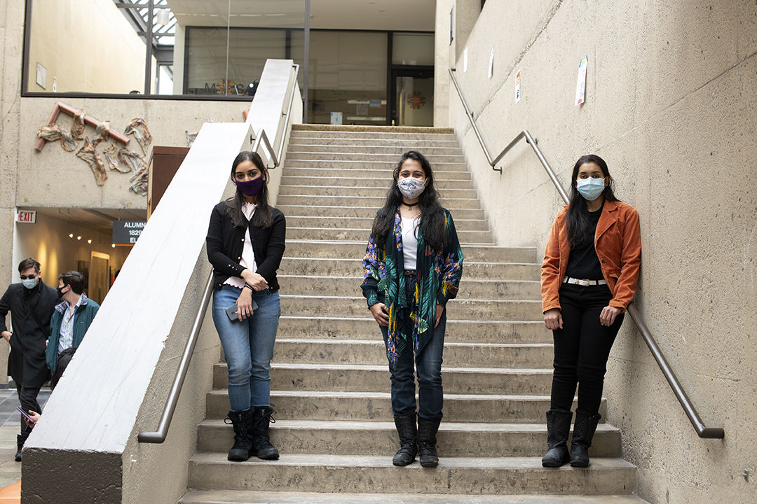 of three masked students standing posing for a photo in a stairway