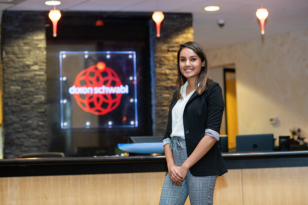 Isha Mehta poses in front of a Dixon Schwabl sign at the agency's office.