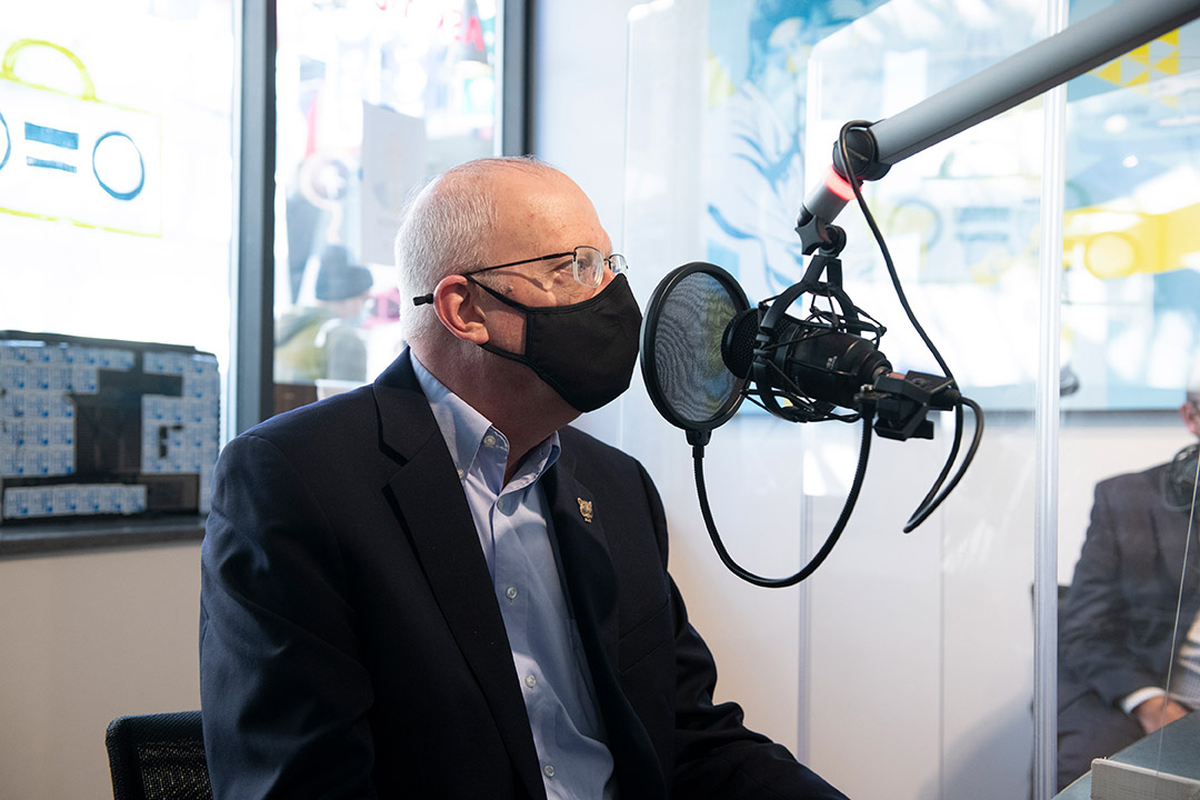 RIT president wearing a facemask and talking into a microphone in a radio station.