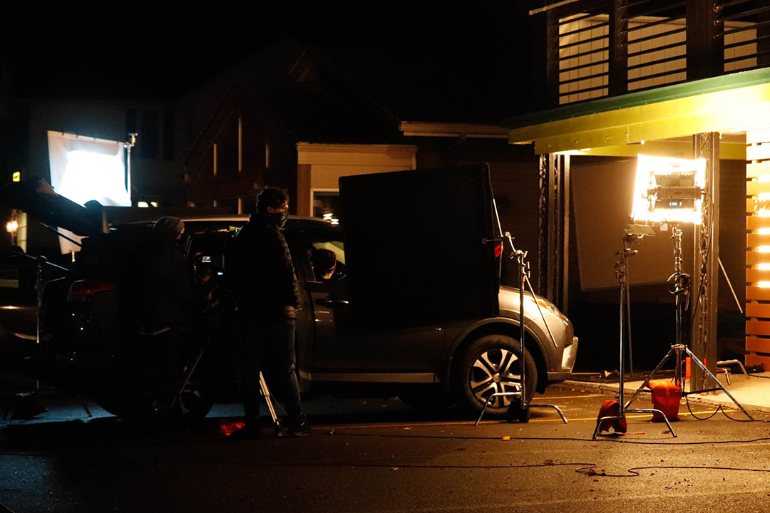 student filmmakers setting up lighting around a parked car.