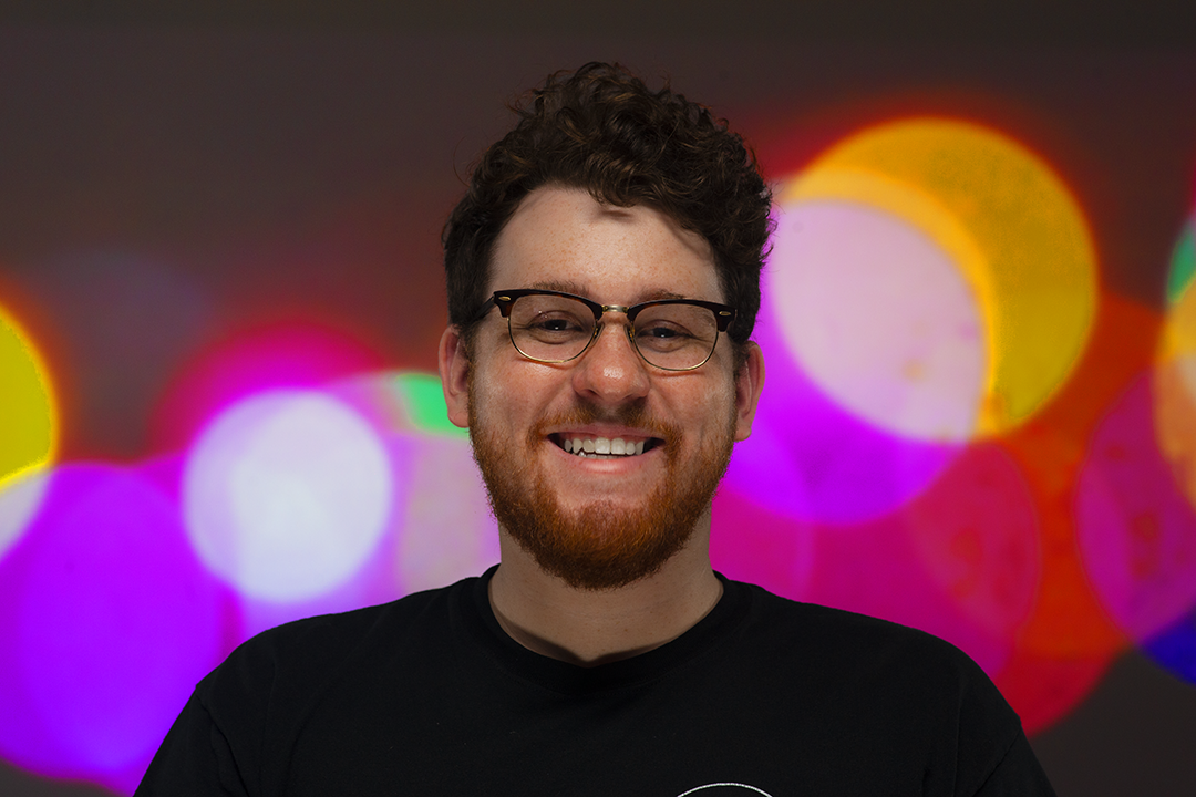 A portrait of Simon Yahn set on a colorful background of an LED panel.
