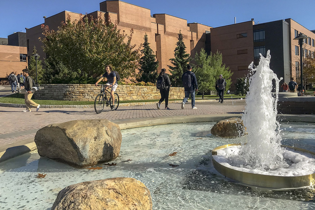 students walking and riding bikes outside near a fountain.