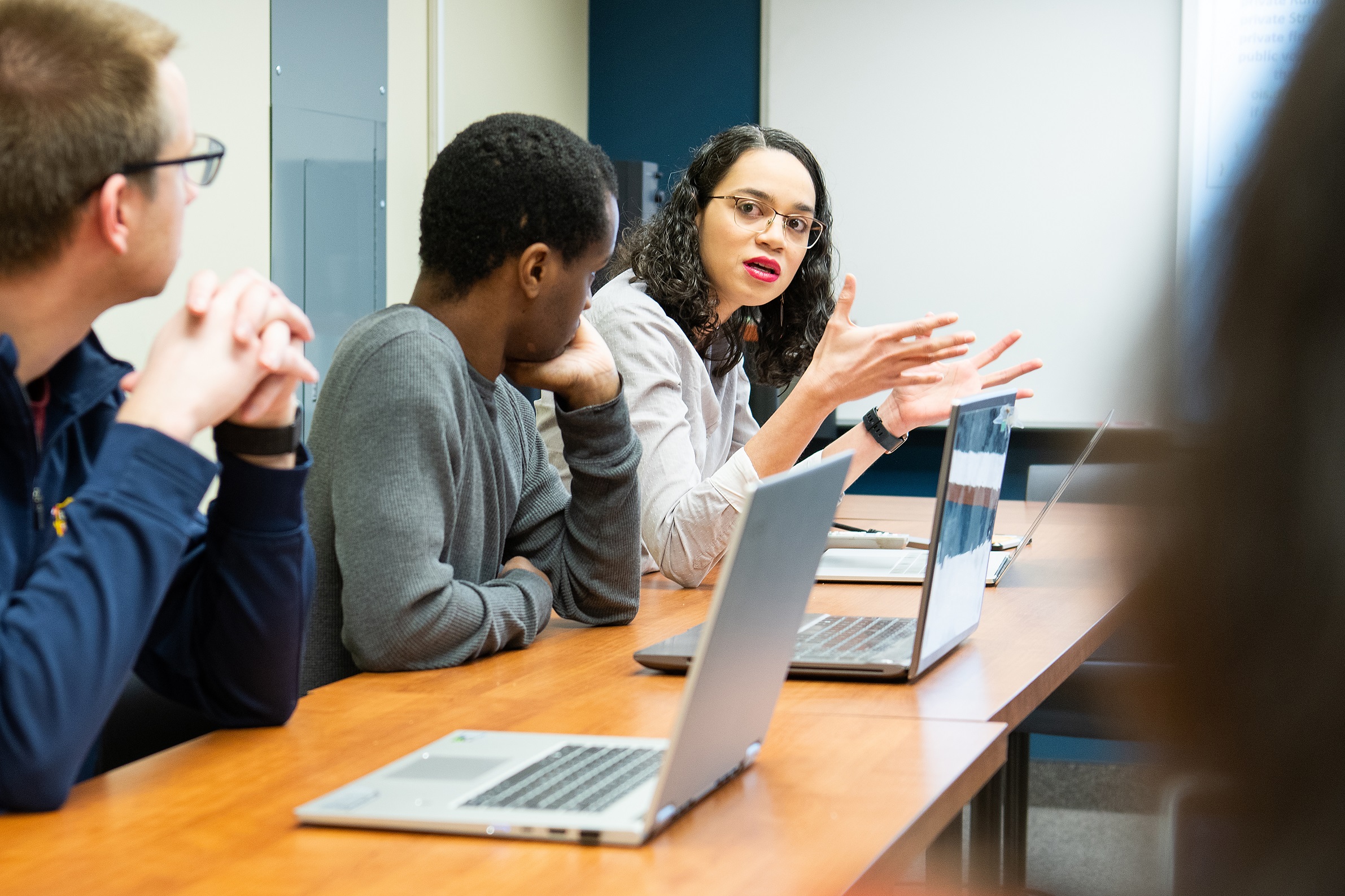 Three people sitting in front of laptops having a discussion.