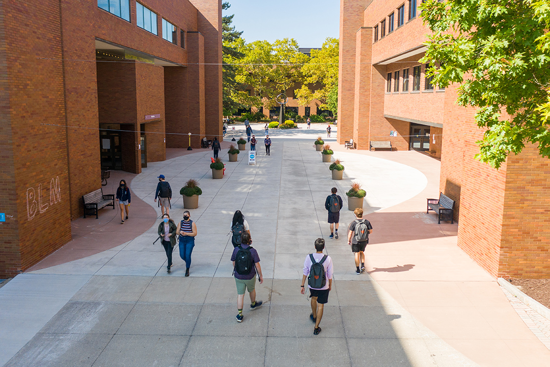 students walking outdoors between two brick buildings.