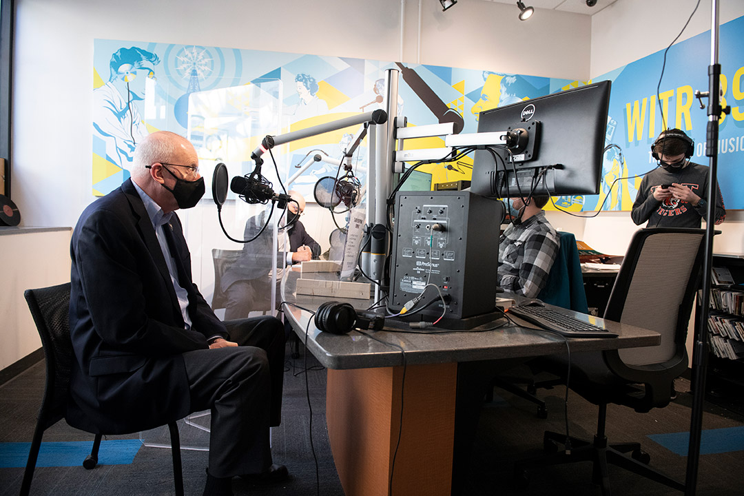 RIT President Munson wearing a mask and speaking into a microphone in a radio station.