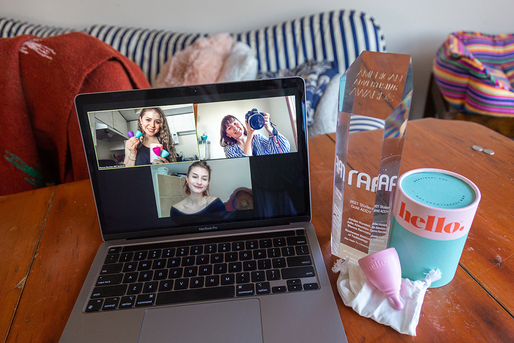laptop on a table showing three students on Zoom, and an award and box for the Hello menstrual cup.
