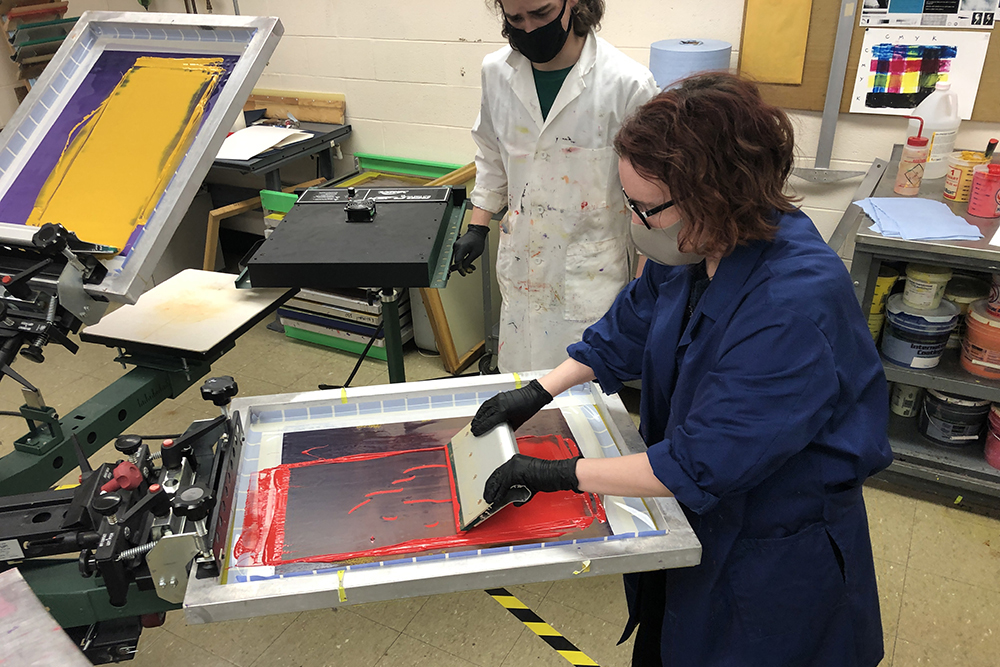 A student manipulates red ink during a screen-printing process.