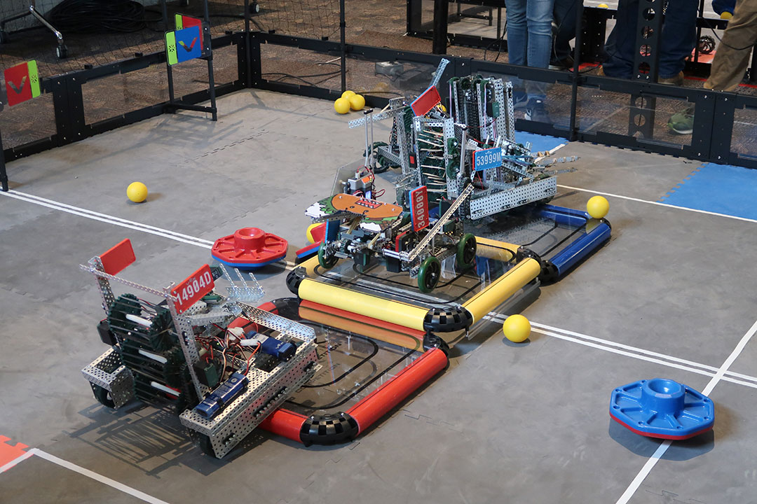 Three hand-crafted robots moving around an enclosed area.