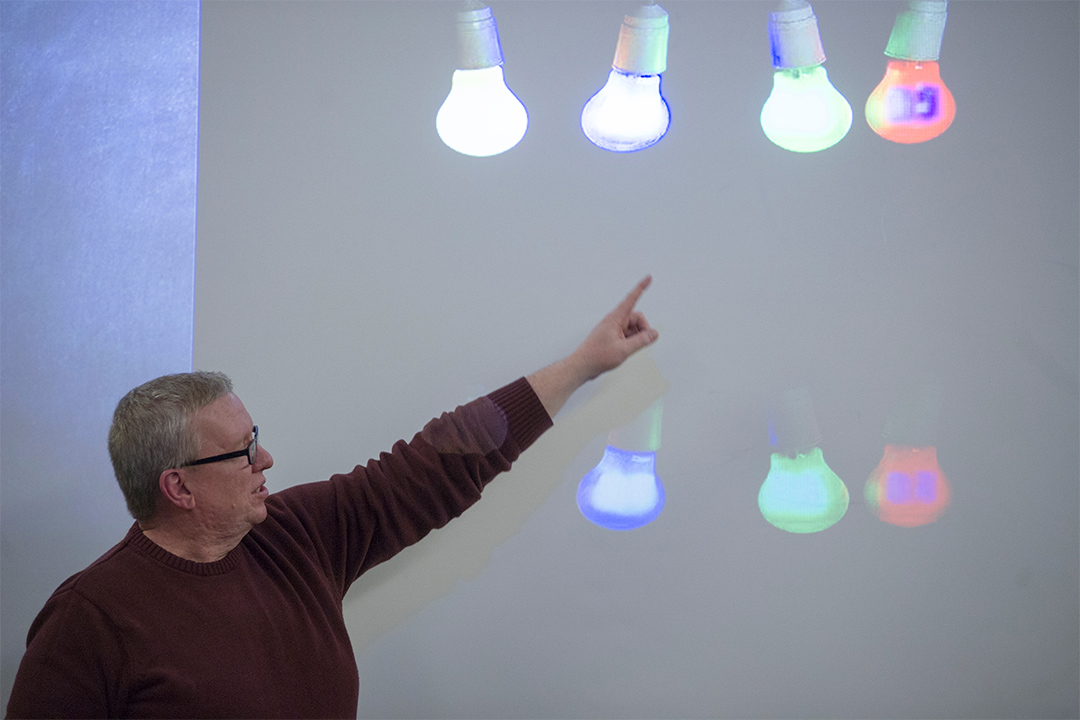 professor pointing to projector image of colored lightbulbs.