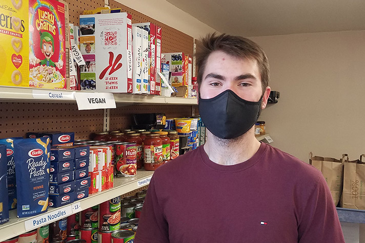 student wearing mask standing in front of shelves of food.
