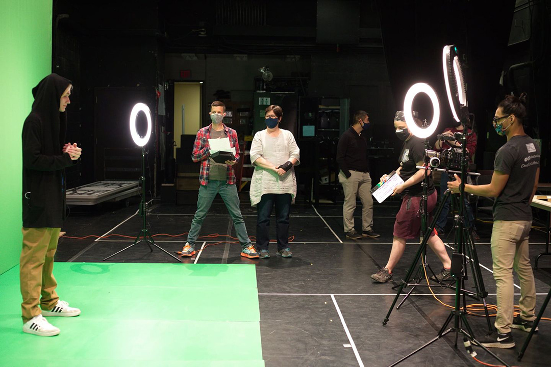 several students filming a student in front of a green screen.