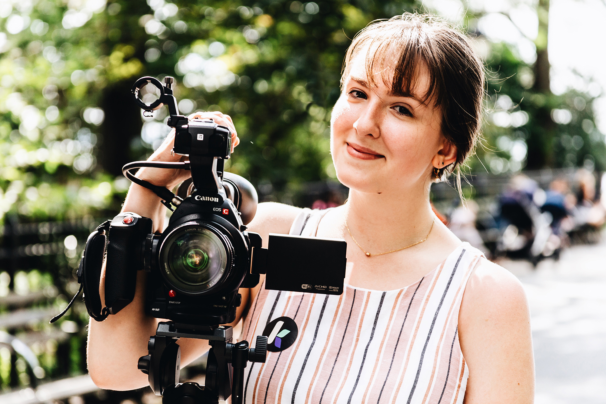 Trisha Pickelhaube stands behind a camera on a tripod.