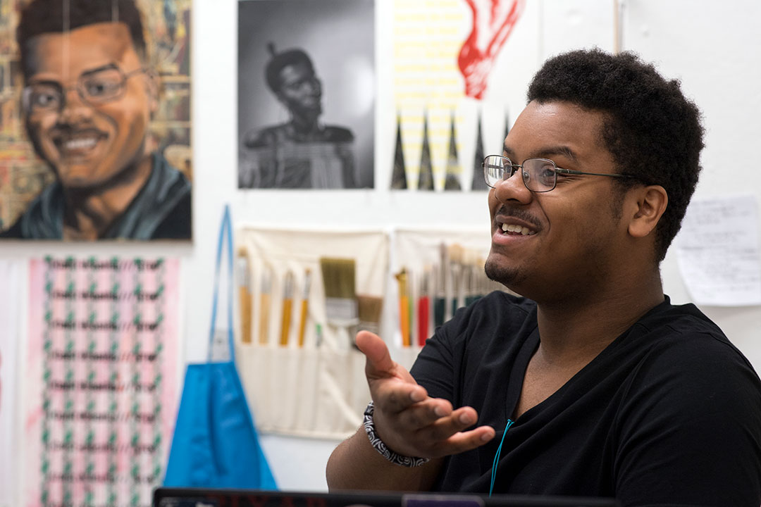 student gestures in front of his artwork.