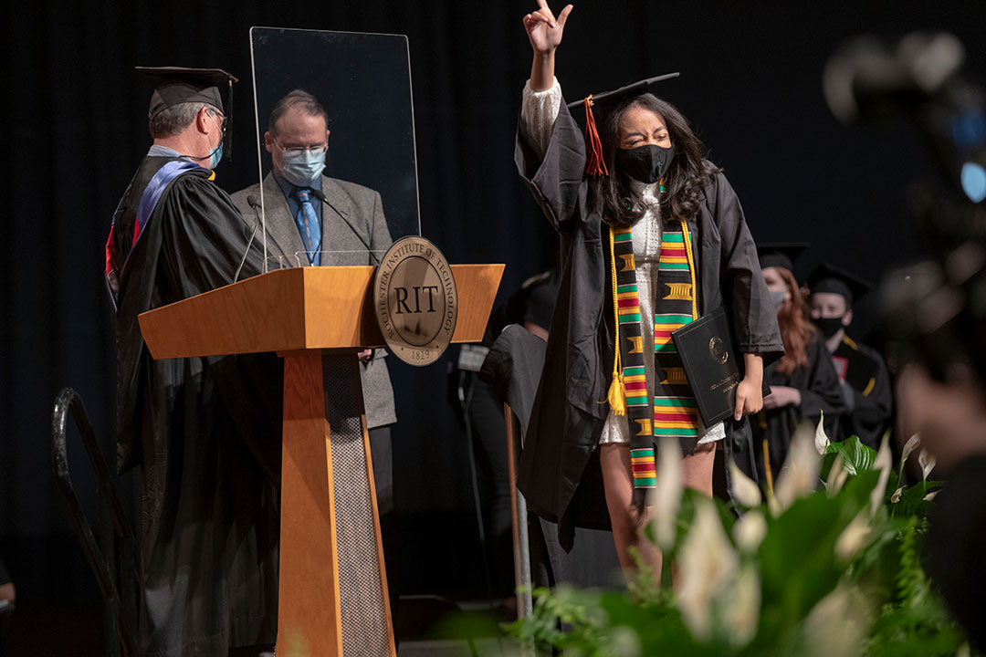 Graduate pointing into the air in celebration while crossing stage.