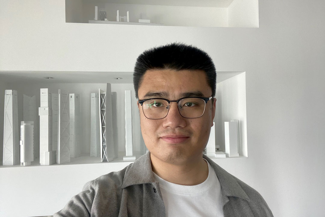 A man wearing glasses poses for a photograph with architectural models.