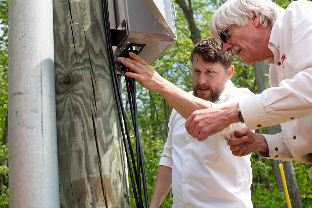 two people install monitoring equipment on a power pole.