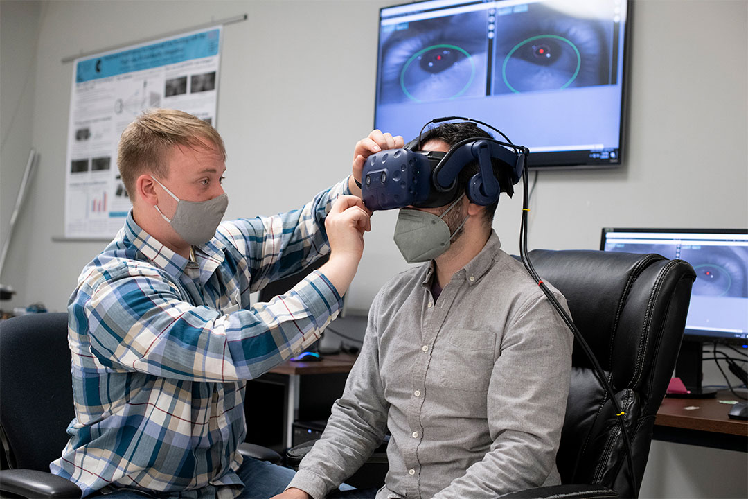 A student adjusts a virtual reality headset on another student.