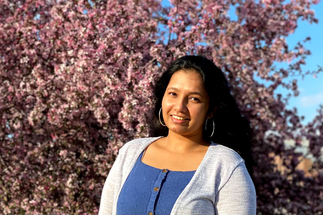 A woman stands in front of a flowering tree.