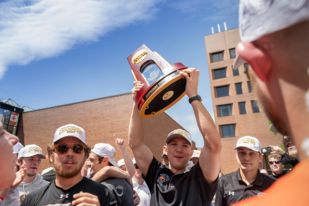 student athlete hoists NCAA trophy into the air.