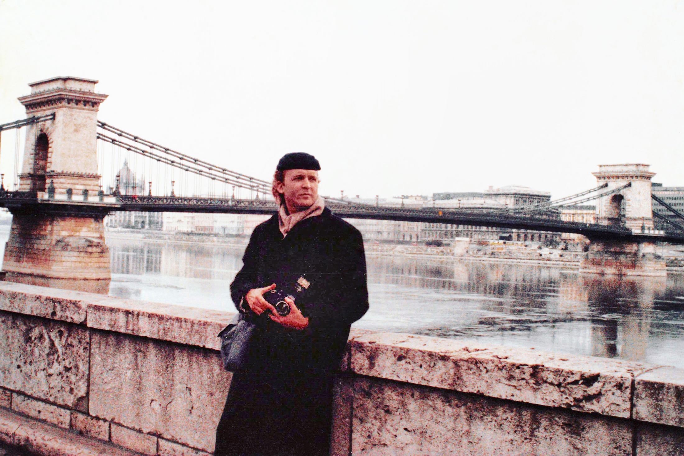 A 1990 photo of Frank Deese holding a camera with water and a bridge in the background.