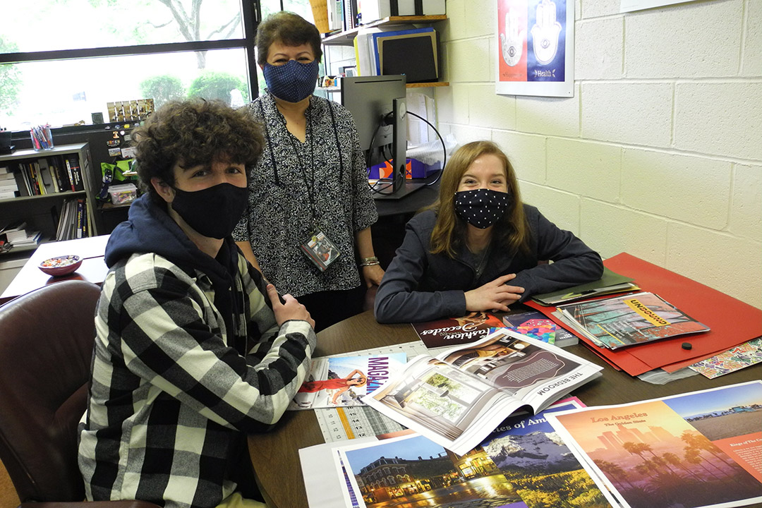 two students and a professor posing with magazine spreads on a table.