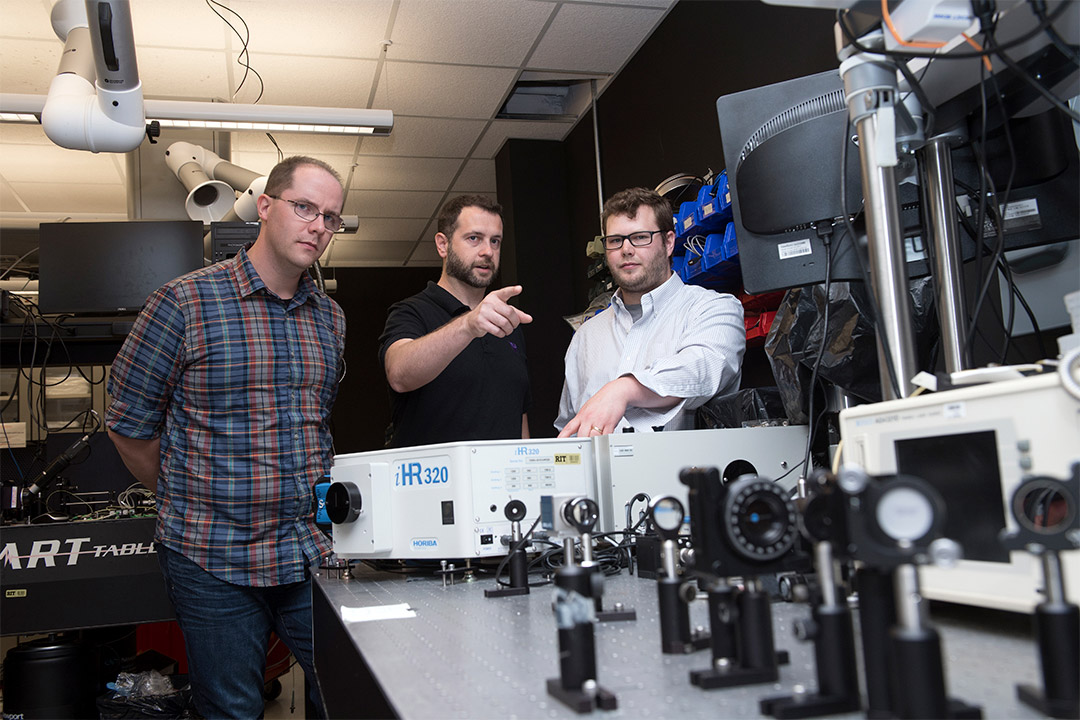 three researchers working with optics and photonics equipment.