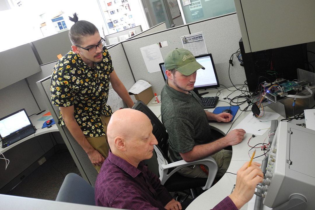 students and professor working at a computer station.