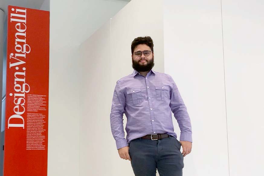 A male student stands next to sign.