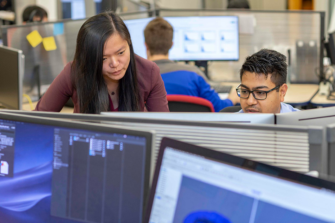 professor looking at student's work in a cluster of computers.