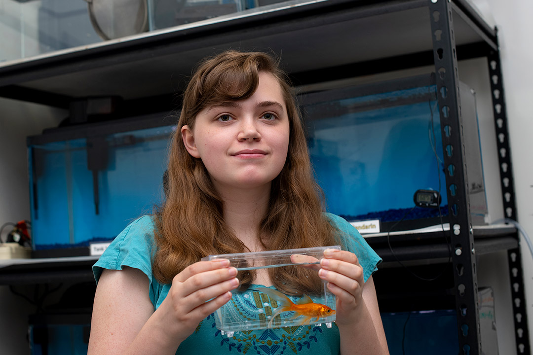 student holding a clear container with a goldfish in it.
