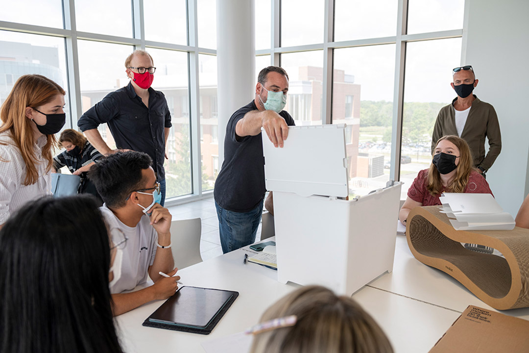 group of people wearing face masks around a table examining a modern cat litter box.