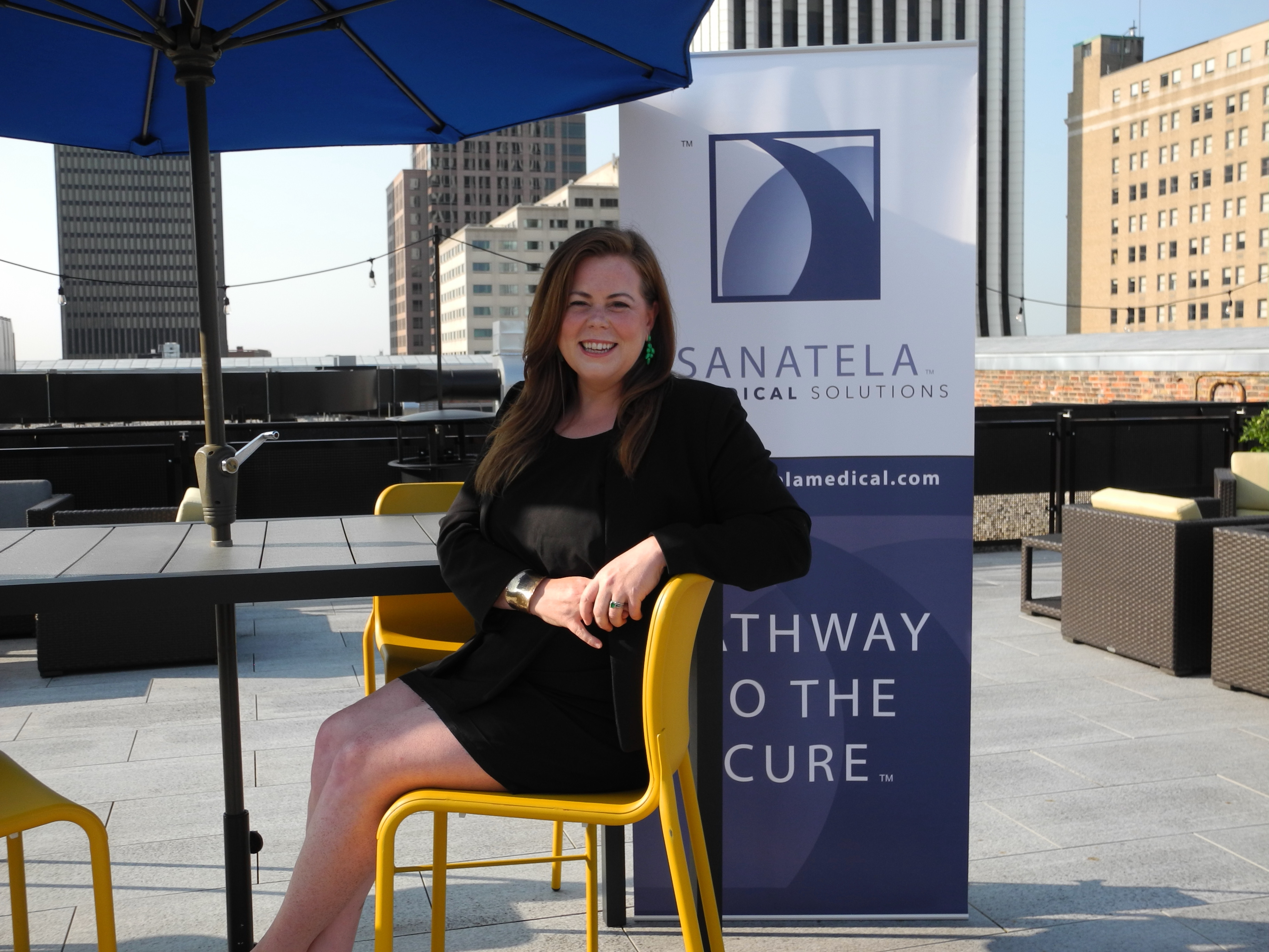 Erin Crowley Ellis sitting at a desk and smiling in front of a sign that says "Sanatela Medical Solutions."