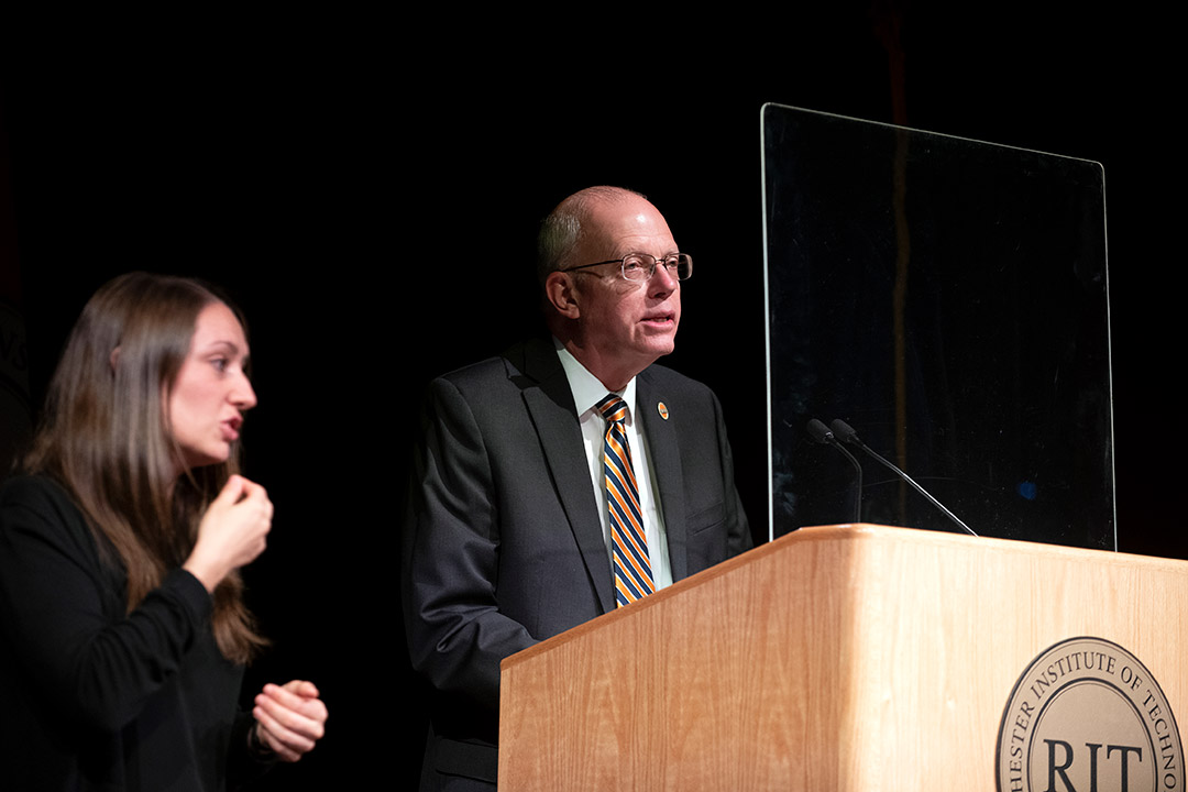 RIT President David Munson speaking at a podium next to an American Sign Language interpreter.