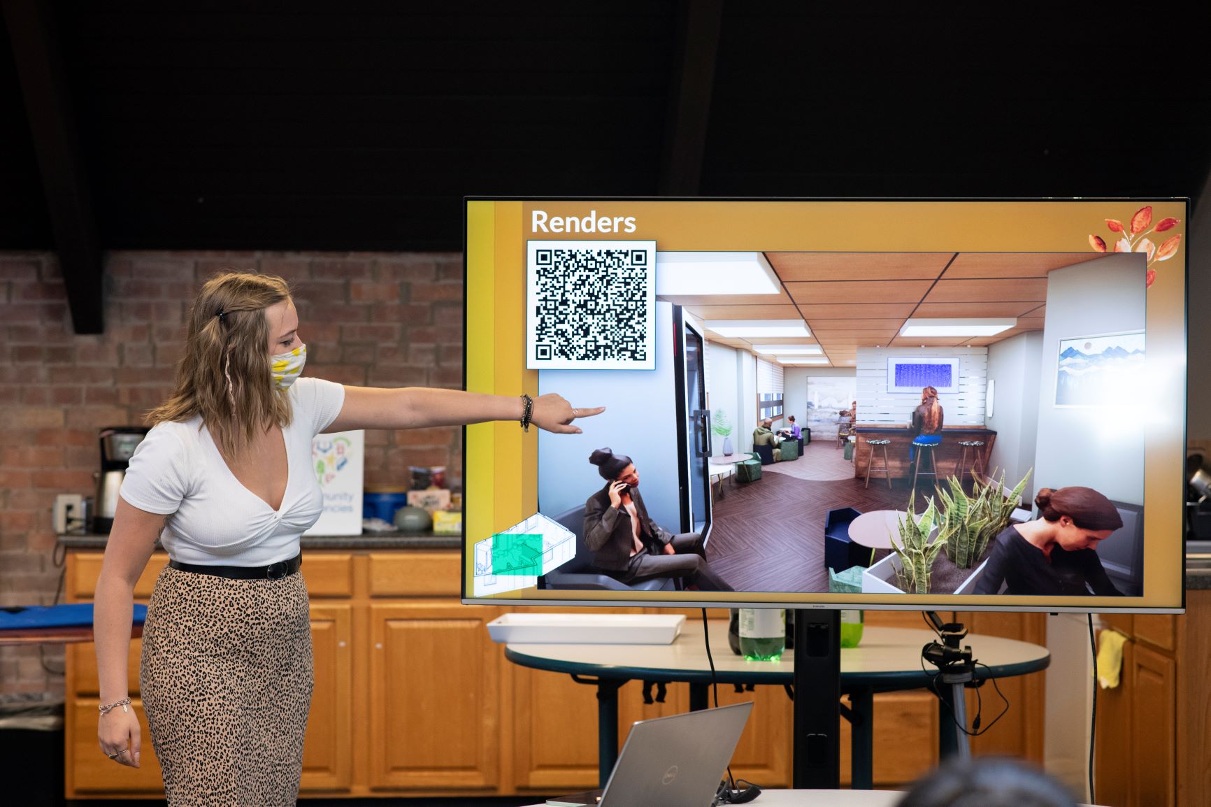 A woman in business attire pointing at a rendering of a medical facility.