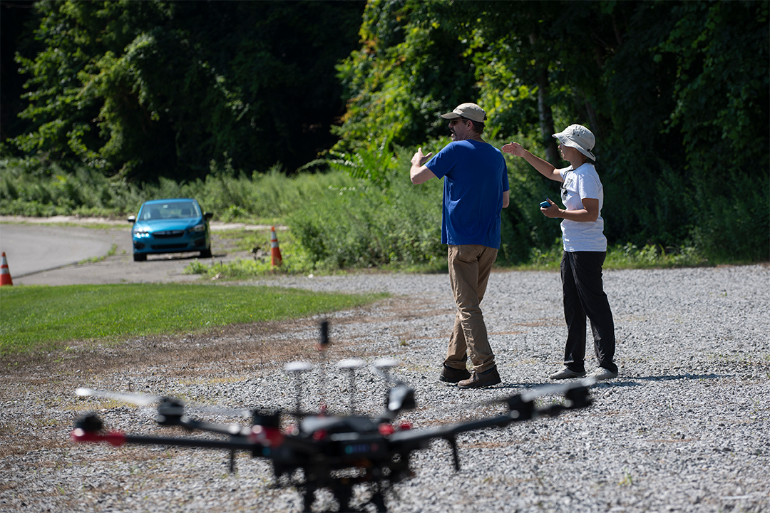 Two people walk next to a drone.