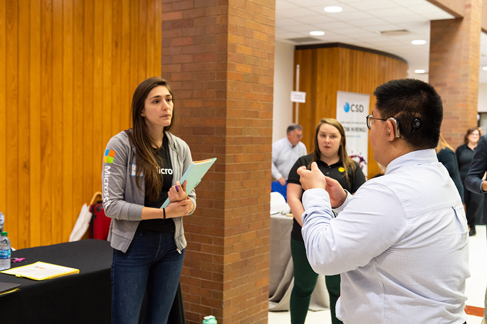 person wearing a cochlear implant using sign language to talk to a recruiter.