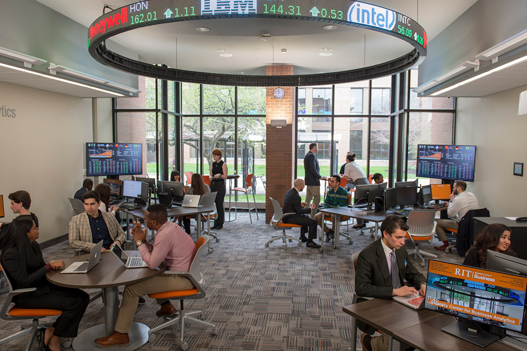 students in a business lab with large, digital stock ticker.