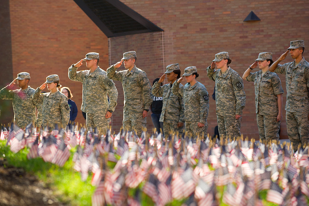 ROTC members saluting in front of a field of small American flags.